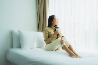 Yatağında kahve fincanı olan Asyalı genç bir kadın.