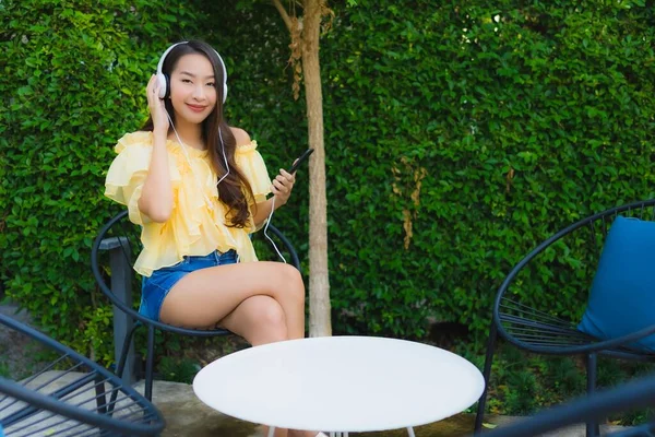 Jovem mulher asiática usando telefone celular inteligente com fone de ouvido para li — Fotografia de Stock