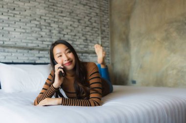 Genç Asyalı kadın yatakta cep telefonu kullanıyor.