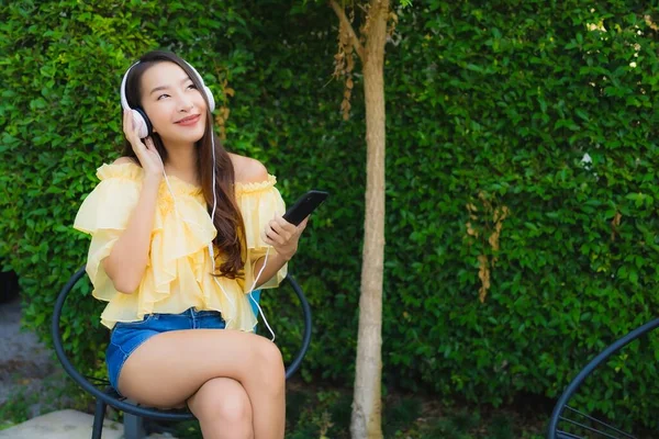 Jovem mulher asiática usando telefone celular inteligente com fone de ouvido para li — Fotografia de Stock