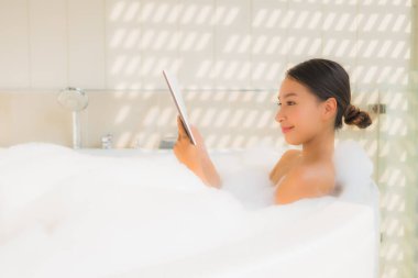 Küvette akıllı cep telefonu kullanan Asyalı genç bir kadının portresi.