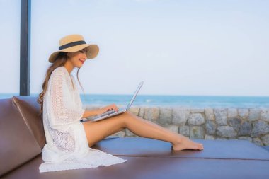 Plaj çevresinde dizüstü bilgisayar kullanan Asyalı genç bir kadının portresi.