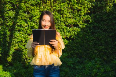 Genç Asyalı kadın açık hava bahçesinde kitap okuyor.