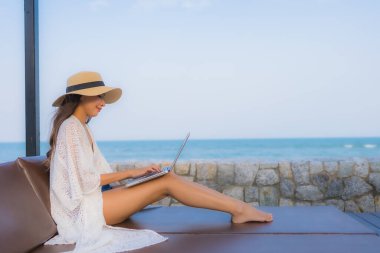 Plaj çevresinde dizüstü bilgisayar kullanan Asyalı genç bir kadının portresi.