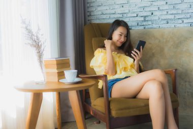 Kahve fincanıyla cep telefonu kullanan Asyalı genç bir kadının portresi.