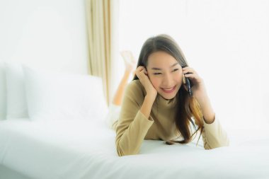 Genç Asyalı kadın yatakta cep telefonu kullanıyor.