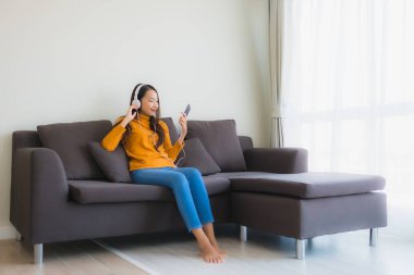 Genç Asyalı kadının portresi kulaklıklı akıllı cep telefonu kullanıyor.