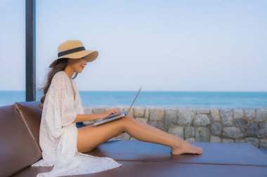 Plaj çevresinde dizüstü bilgisayar kullanan Asyalı genç bir kadının portresi.