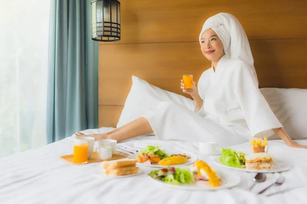 照片中年轻的亚洲女人躺在床上，在卧室里吃早餐 — 图库照片