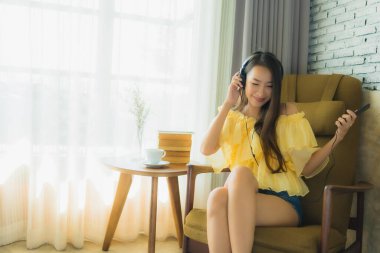 Portre genç Asyalı kadın sandalyeye otur ve cep telefonuyla müzik dinle.