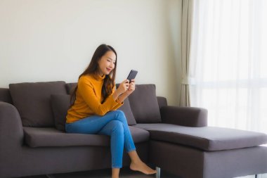 Kanepede akıllı cep telefonu kullanan Asyalı genç bir kadının portresi.