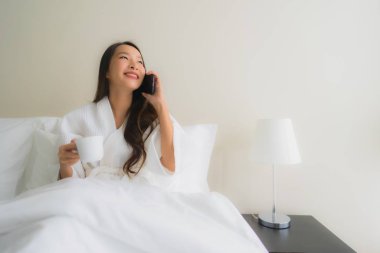 Kahve fincanı ve cep telefonuyla güzel Asyalı genç kadınların portresi. 