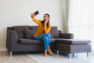 Kanepede akıllı cep telefonu kullanan Asyalı genç bir kadının portresi.