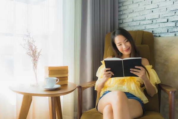 Asyalı genç bir kadının portresi. Kanepeye oturup kitap okuyor. — Stok fotoğraf