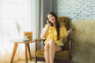 Portre genç Asyalı kadın sandalyeye otur ve cep telefonuyla müzik dinle.