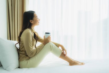 Yatağında kahve fincanı olan Asyalı genç bir kadın.