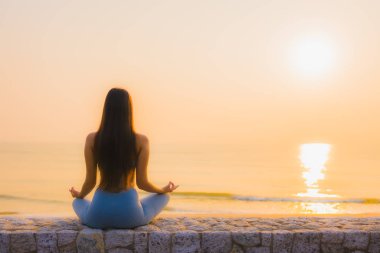 Genç Asyalı kadının portresi sağlık için gün doğumunda deniz kıyısı okyanusunda meditasyon yapıyor.