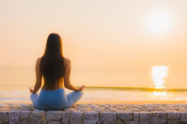 Genç Asyalı kadının portresi sağlık için gün doğumunda deniz kıyısı okyanusunda meditasyon yapıyor.