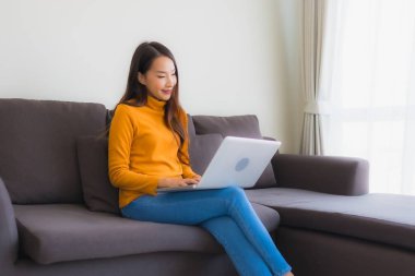 Genç Asyalı bir kadının oturma odasında çalışmak için dizüstü bilgisayar defteri kullanmasının portresi.