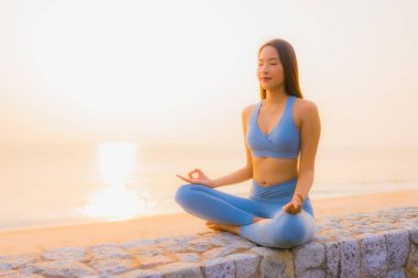 Genç Asyalı kadının portresi sağlık için gün doğumunda deniz kıyısı okyanusunda meditasyon yapıyor.
