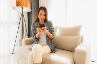 Konuşan cep telefonu kullanan ve oturma odasındaki koltukta oturan güzel Asyalı kadınların portresi.
