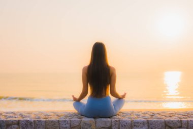 Genç Asyalı kadının portresi sağlık için gün doğumunda deniz kıyısı okyanusunda meditasyon yapıyor.