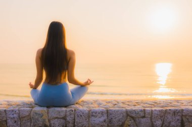 Genç Asyalı kadının portresi sağlık için gün doğumunda deniz kıyısı okyanusunda meditasyon yapıyor.
