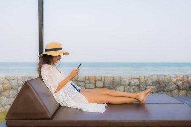 Açık deniz okyanusunda akıllı cep telefonu kullanan Asyalı genç bir kadının portresi.