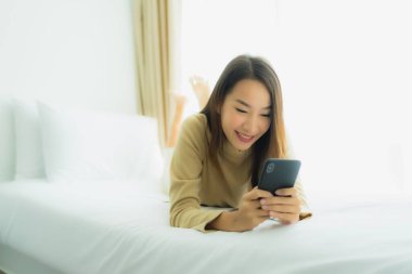 Genç Asyalı kadın yatak odasının iç kısmında cep telefonu kullanıyor.