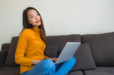 Genç Asyalı bir kadının oturma odasında çalışmak için dizüstü bilgisayar defteri kullanmasının portresi.