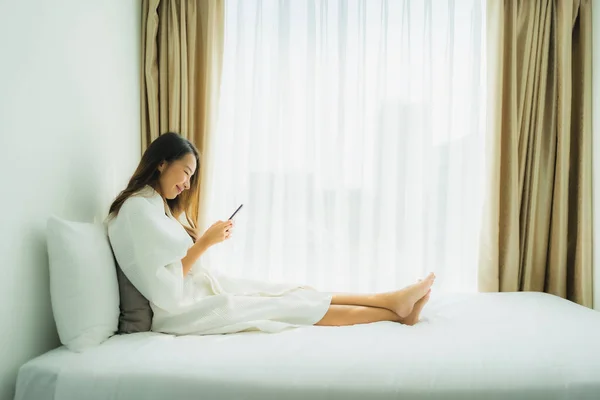 Young asian woman using mobile smart phone on bed in bedroom interior