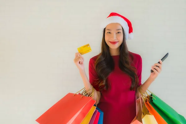 肖像画の美しい若いアジアの女性は ショッピングバッグスマート携帯電話とクレジットカードでクリスマスサンタの帽子を着用 — ストック写真