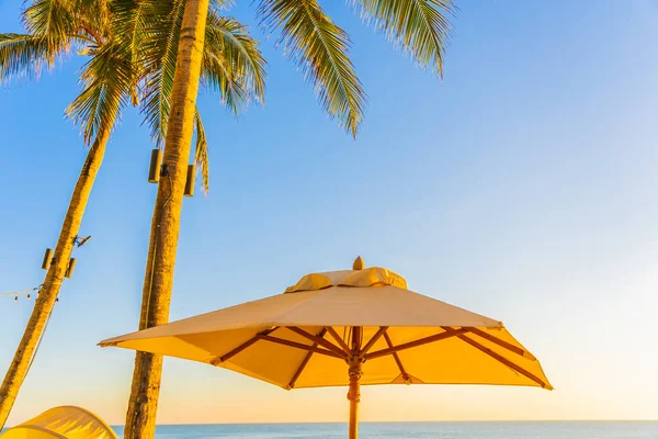 日落或日出时带棕榈树环抱海滩海的美丽热带自然保护伞椅 供游玩 — 图库照片