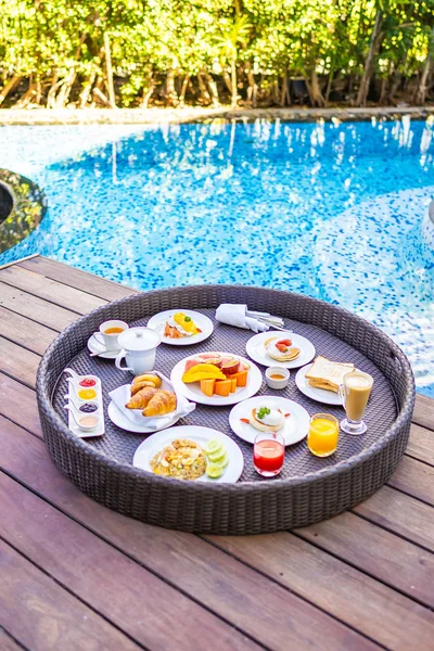 屋外スイミングプールの周りに浮かぶ朝食トレイパンフルーツ卵コーヒーカップとジュース — ストック写真