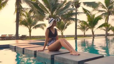 Güzel Asyalı bir kadının, tatil için otel tatil beldesinde yüzme havuzunda dinlendiği görüntüler.