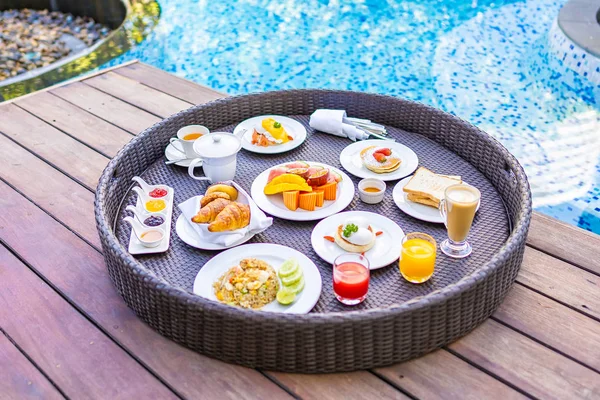 屋外スイミングプールの周りに浮かぶ朝食トレイパンフルーツ卵コーヒーカップとジュース — ストック写真