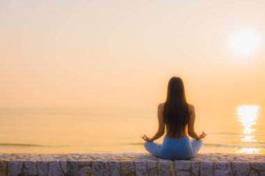 Genç Asyalı kadının portresi sağlık için gün doğumunda deniz kıyısı okyanusunda meditasyon yapıyor.