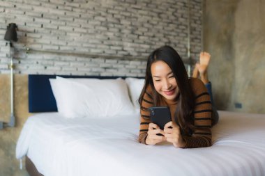 Genç Asyalı kadın yatak odasının iç kısmında cep telefonu kullanıyor.