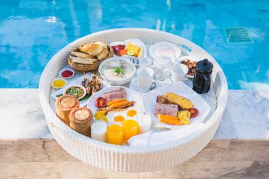 Kızarmış yumurta omletli, jambonlu, meyveli, sütlü kahveli ve yüzme havuzlu bir tepside yüzen kahvaltı.