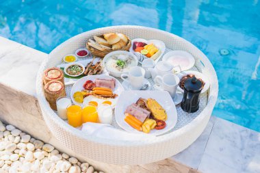 Kızarmış yumurta omletli, jambonlu, meyveli, sütlü kahveli ve yüzme havuzlu bir tepside yüzen kahvaltı.