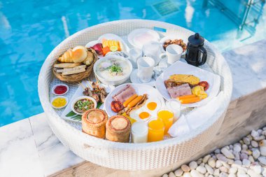 Kızarmış yumurta omletli, jambonlu, meyveli, sütlü kahveli ve yüzme havuzlu bir tepside yüzen kahvaltı.