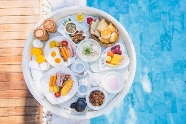 Kızarmış yumurta omletli, jambonlu, meyveli, sütlü kahveli ve yüzme havuzlu bir tepside yüzen kahvaltı.