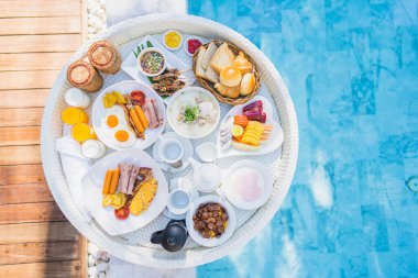 Kızarmış yumurta omletli, jambonlu, meyveli, sütlü kahveli ve yüzme havuzlu bir tepside yüzen kahvaltı.