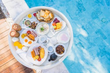 Kızarmış yumurta omletli, jambonlu, meyveli, sütlü kahveli ve yüzme havuzlu bir tepside yüzen kahvaltı.