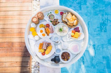 Kızarmış yumurta omletli, jambonlu, meyveli, sütlü kahveli ve yüzme havuzlu bir tepside yüzen kahvaltı.