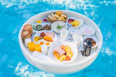 Kızarmış yumurta omletli, jambonlu, meyveli, sütlü kahveli ve yüzme havuzlu bir tepside yüzen kahvaltı.