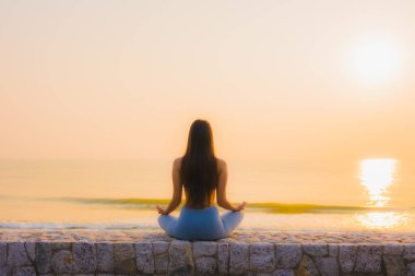 Genç Asyalı kadının portresi sağlık için gün doğumunda deniz kıyısı okyanusunda meditasyon yapıyor.