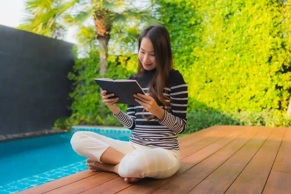 Portrait young asian woman read book around outdoor swimming pool in hotel resort