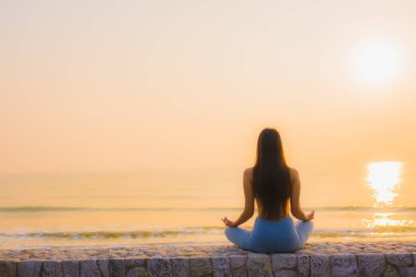 Genç Asyalı kadının portresi sağlık için gün doğumunda deniz kıyısı okyanusunda meditasyon yapıyor.