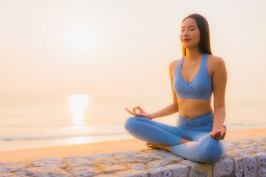 Genç Asyalı kadının portresi sağlık için gün doğumunda deniz kıyısı okyanusunda meditasyon yapıyor.